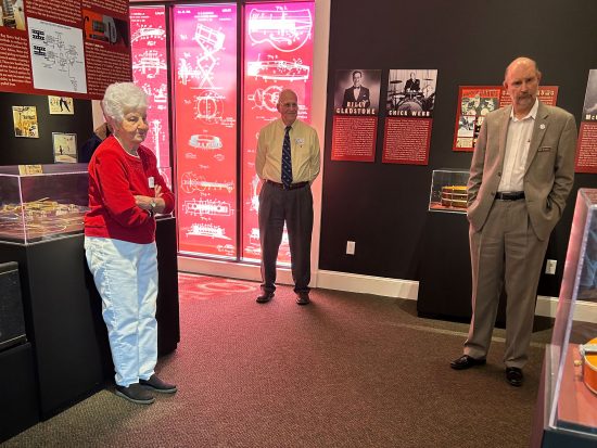 Two men and a woman standing around at the Gretsch exhibit.