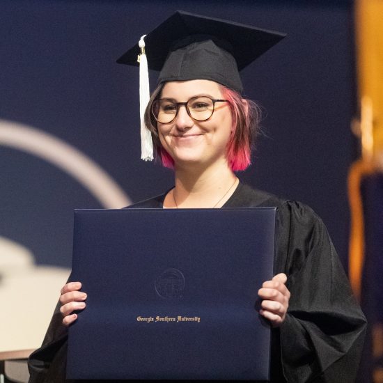 Graduate smiling while holding college diploma.