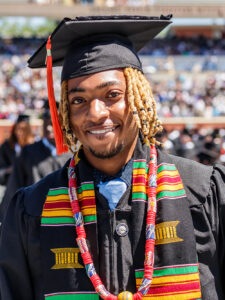 Young black man adorned in graduating robes with cap, gown, and academic regalia.