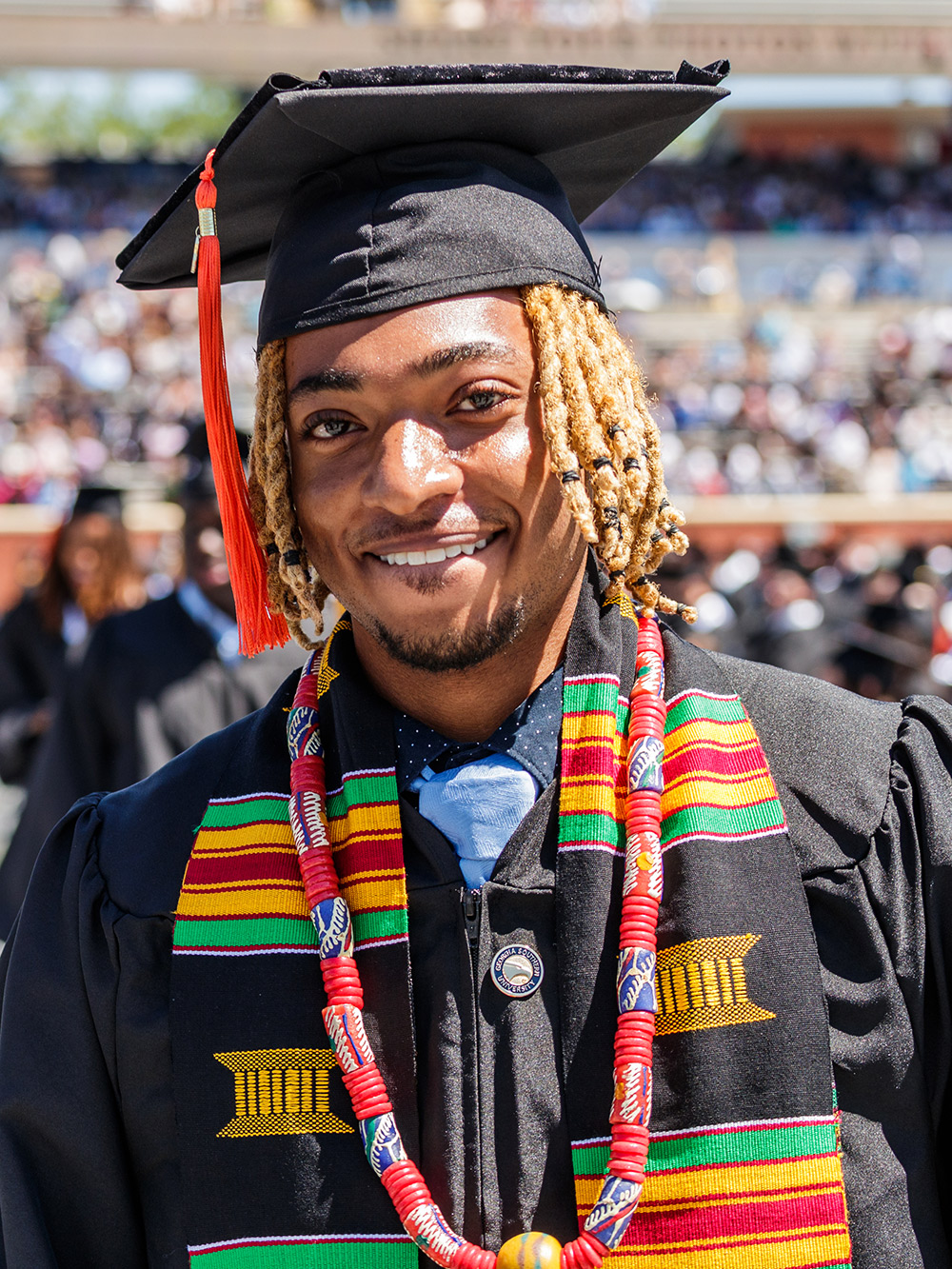 Young black man adorned in graduating robes with cap, gown, and academic regalia.