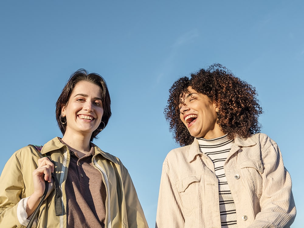 Two students smiling and laughing outdoors under a clear blue sky, enjoying a sunny day at Georgia Southern University.