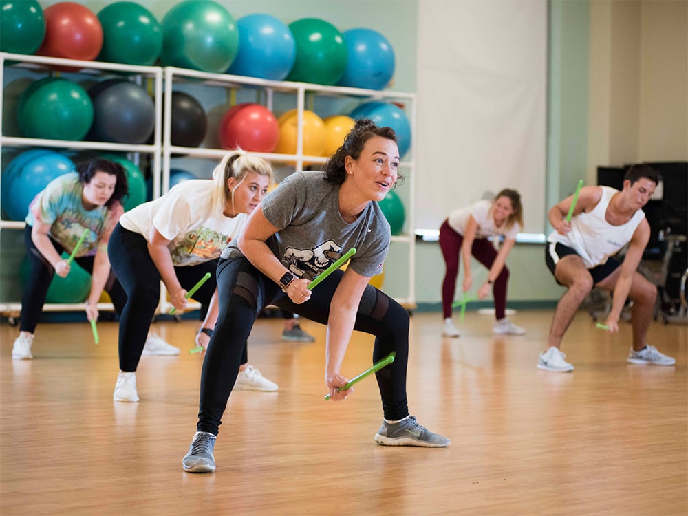 Georgia Southern students participating in a group fitness class using drumsticks in a campus recreation center.
