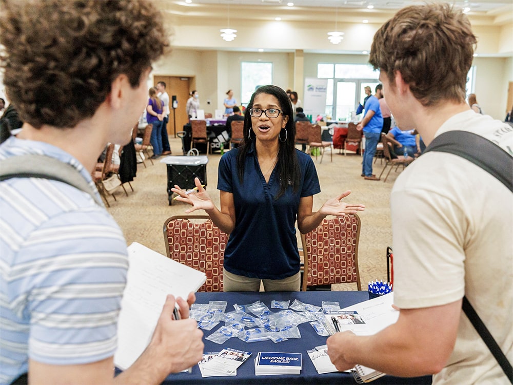 Georgia Southern students speaking with staff at a campus involvement fair table with brochures and name tags displayed.