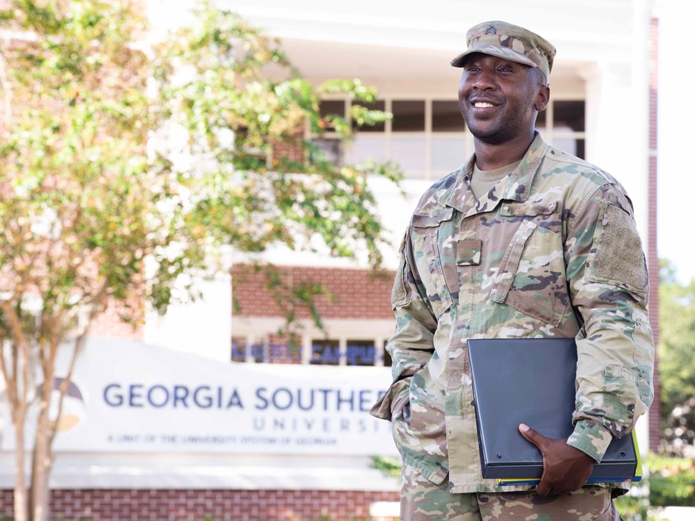 Georgia Southern student in military uniform holding a binder and smiling outside a campus building.