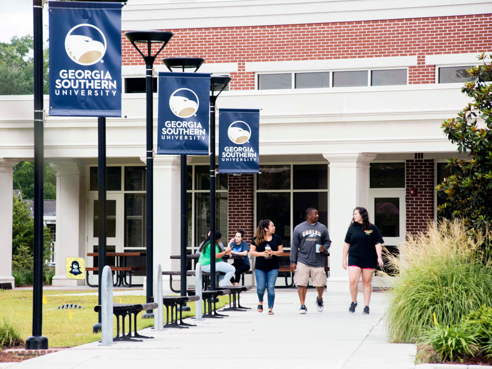 Georgia Southern University students walking and talking outside a campus building with branded banners displayed.