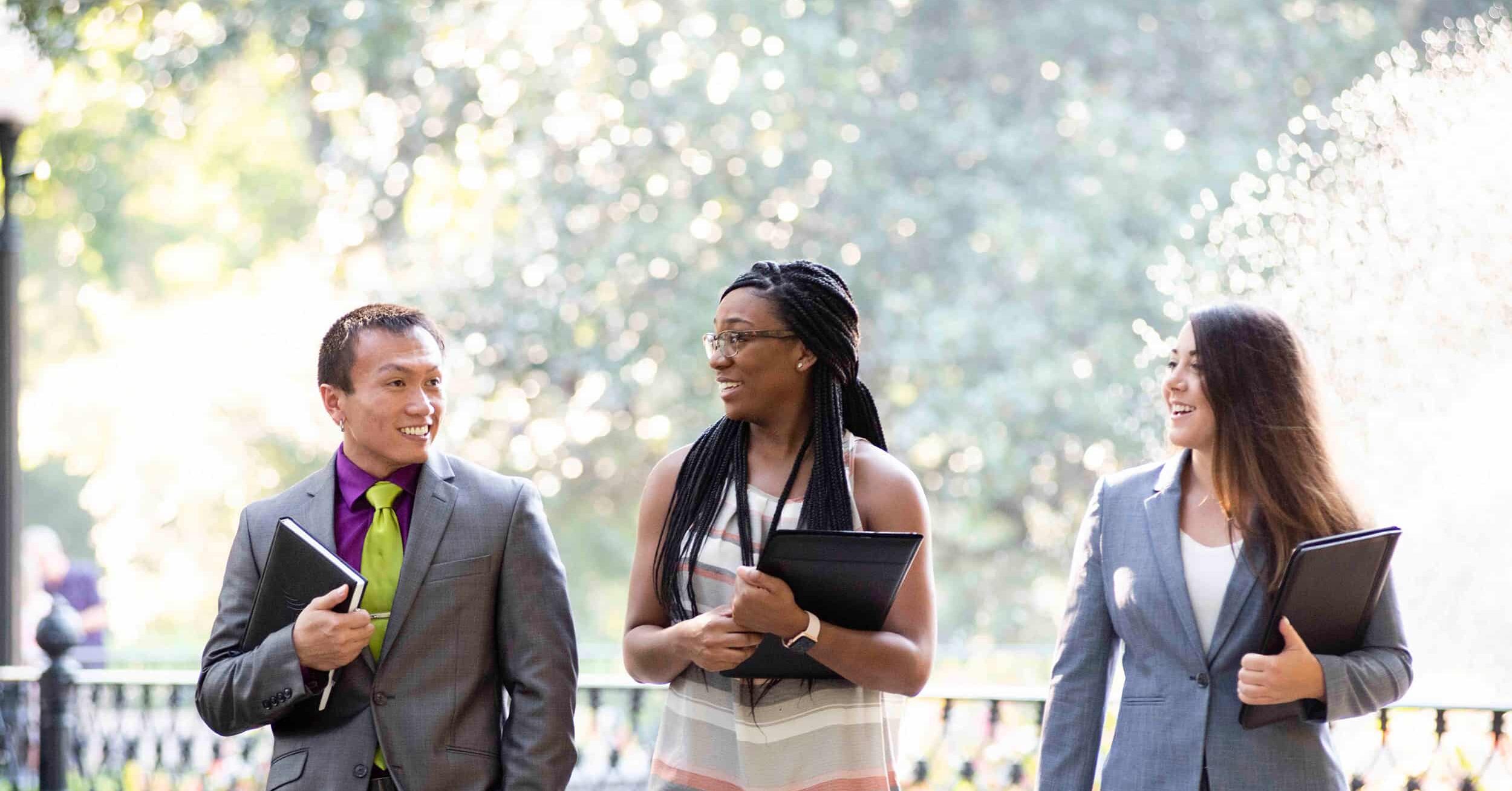 three Parker College students walking outside in business clothes holding notebooks