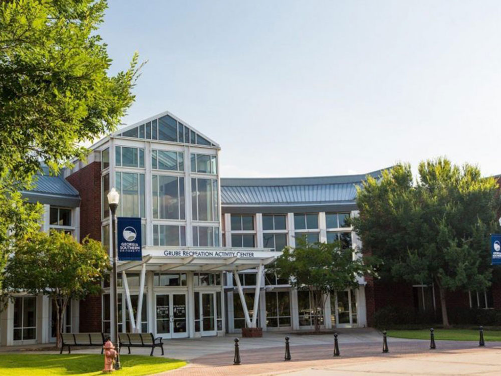 A modern building with large glass windows and a sign reading Recreation Activity Center at the entrance, surrounded by trees and a clear sky in the background.