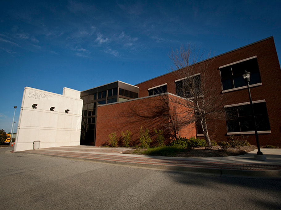 A modern brick and white concrete building with large windows and minimal landscaping, photographed under a clear blue sky.