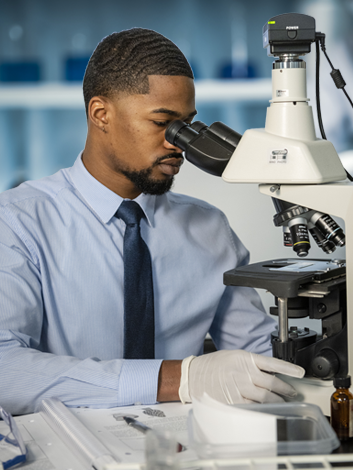 Young professional in suit and tie examines a specimen under a microscope for experiential preparation for a successful career.