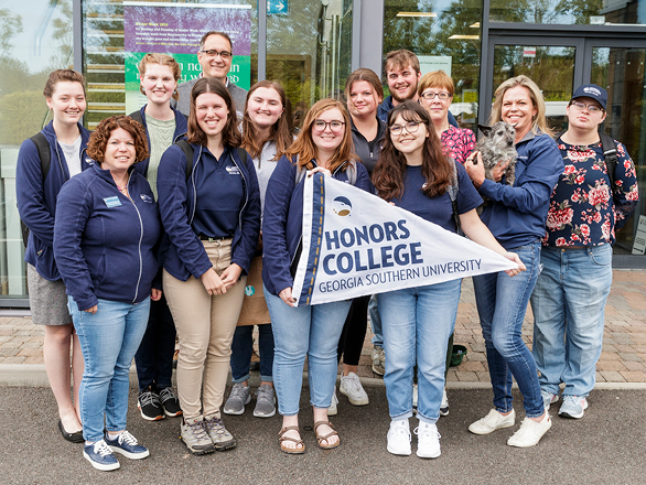 A group of students and staff from Georgia Southern's Honors College stand outdoors with a pennant