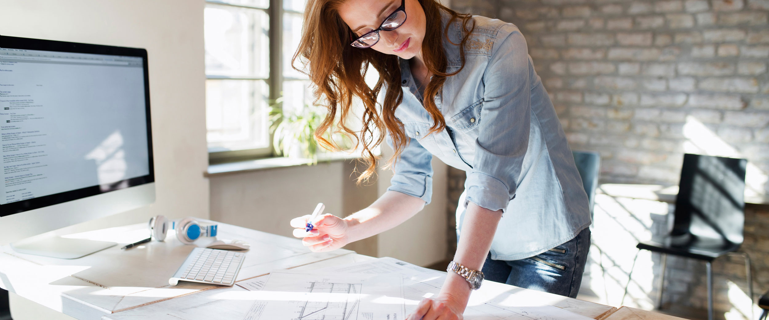 In a studio space at Georgia Southern, a B.S. in Interior Design student leans over a desk with a computer to work on a drawing