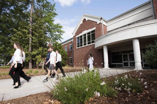 Students walking outside University Hall, surrounded by trees and landscaping.