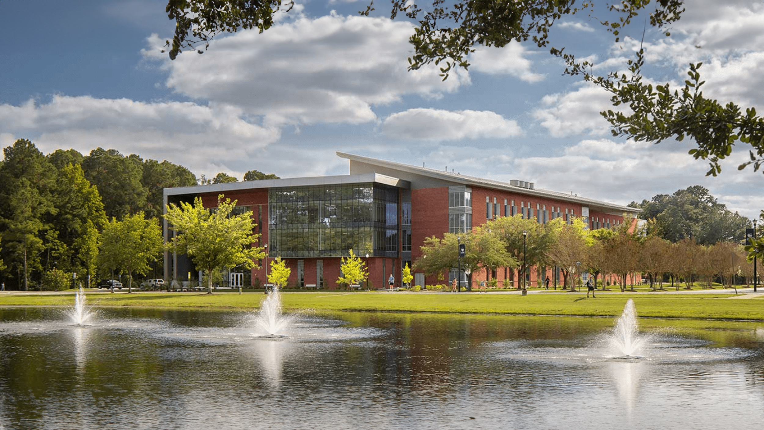 Georgia Southern campus building with glass windows behind a pond and fountains, surrounded by trees and a walking path.