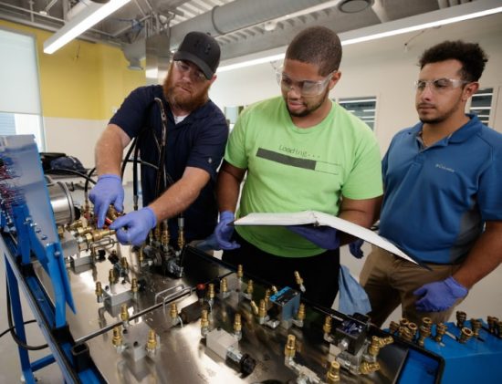 Students collaborating on machinery with safety gear in Paulson Summer Apprenticeship.