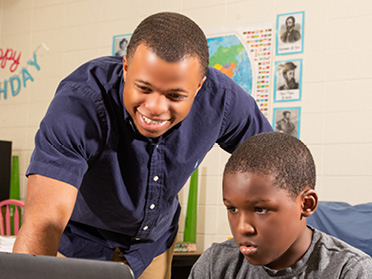 A student in Georgia Southern's Counselor Education, M.Ed. Program instructs a child on a computer.