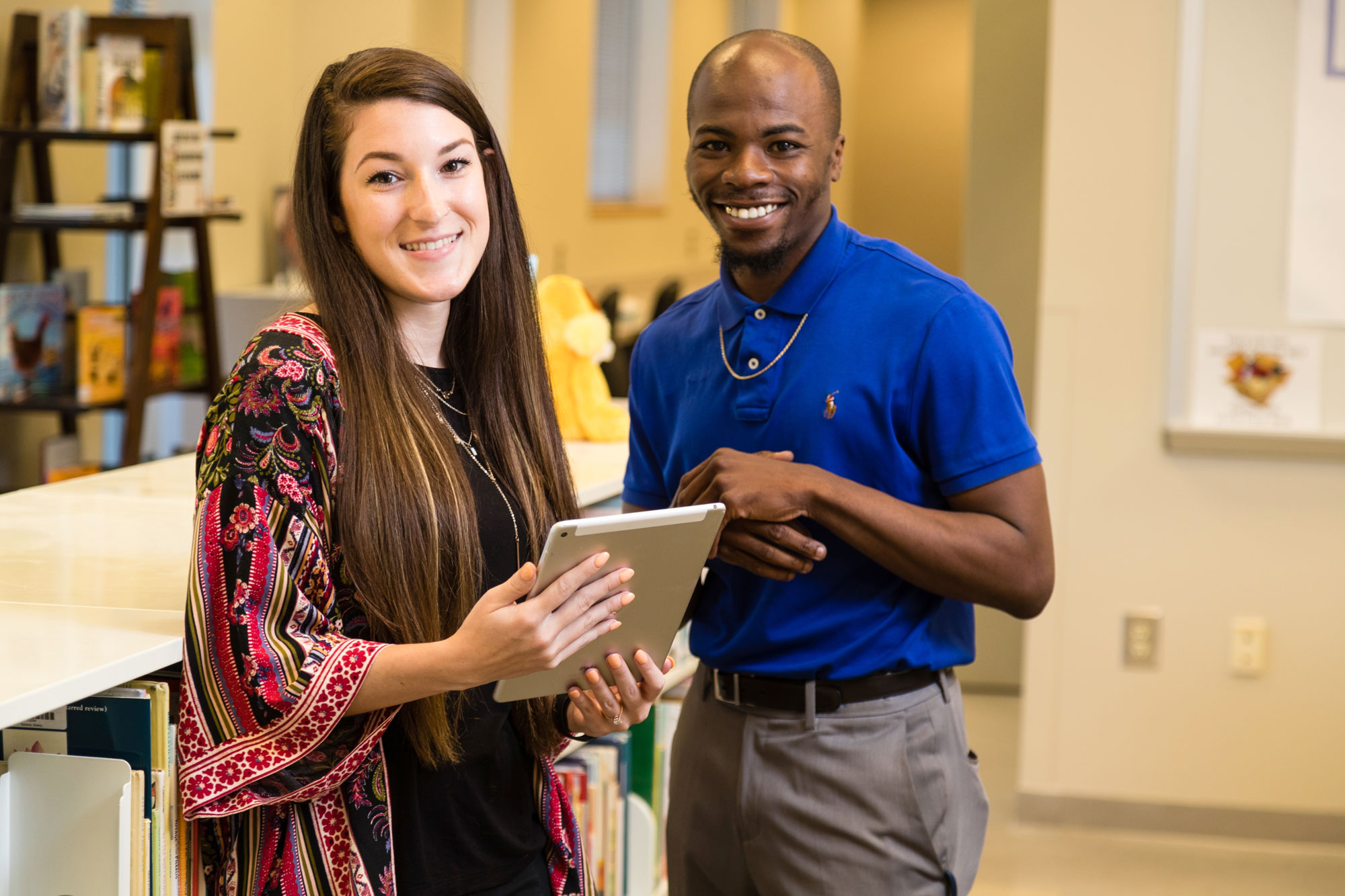 Two students stand together among a library of books and files.