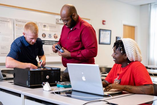 Three students working together with a laptop and hard drive to learn electrical and computer engineering.