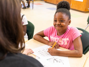 A student sitting at a desk smiles upward at a student teacher from Georgia Southern's Department of Elementary and Special Education