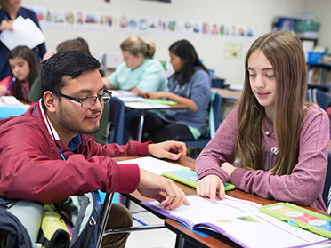 A student teacher from Georgia Southern's Department of Leadership, Technology and Human Development and a student sitting at a desk point to sections of a book