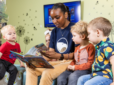 A student reads to four toddler-age children.