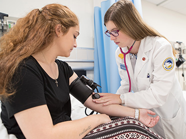 Wearing a lab coat, a student from Georgia Southern's Department of Nursing uses a stethoscope to listen to another student's pulse