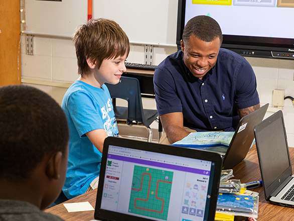 An adult learner teaches children how to code in classroom setting after earning a professional certificate.
