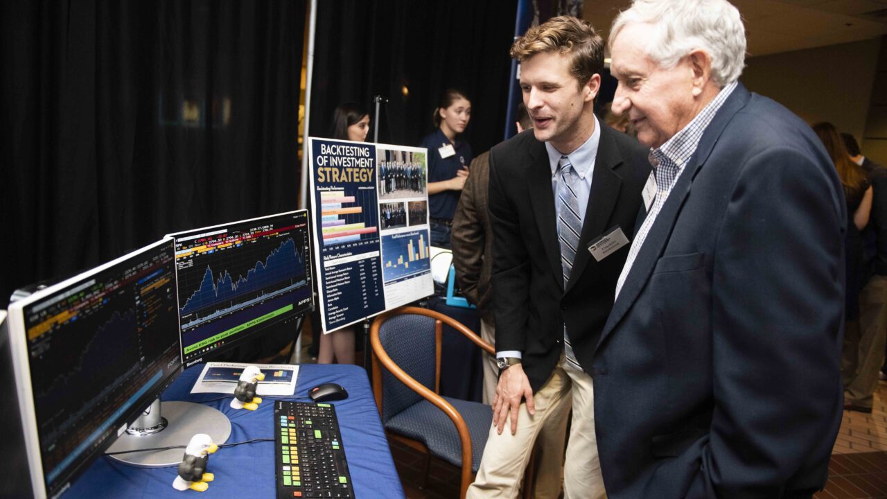 Attendees at 1906 Society Event activation look on to screens a graphs of investment strategy.