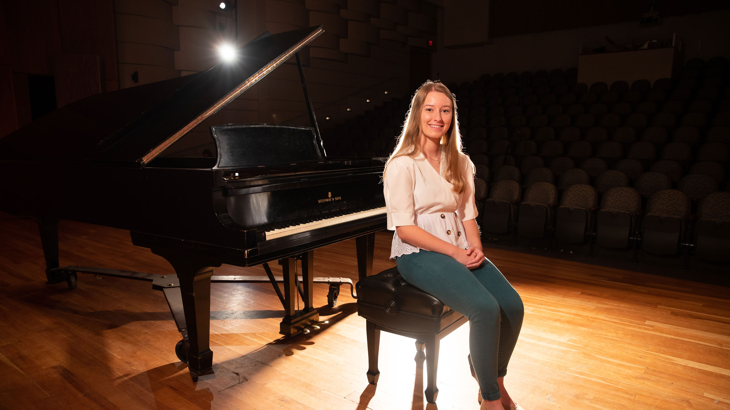 A Georgia Southern student poses in front of a grand piano in a concert hall before a solo performance.