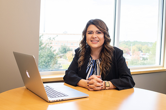Georgia Southern student smiles at a table with laptop in the Masters in Criminal Justice Program.