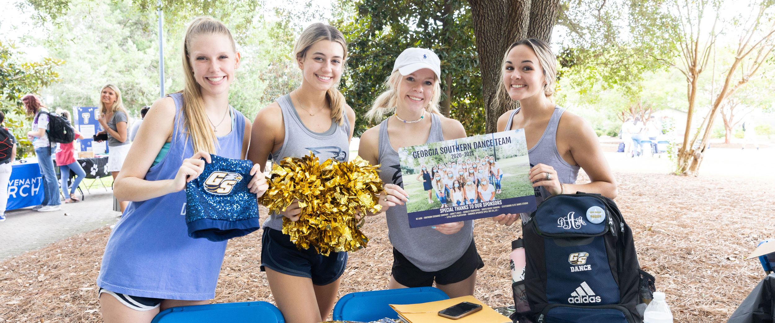 Four students promote Georgia Southern's dance team with a poster and pom-poms