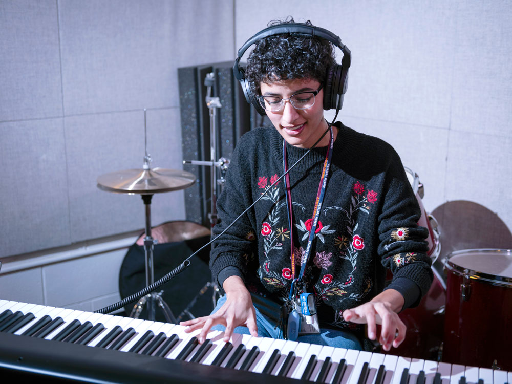 A Georgia Southern student in headphones plays keyboard with a drum set behind him to finalize his musical composition.