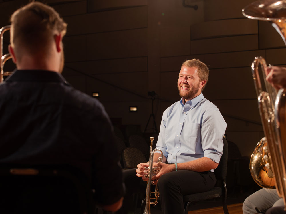 A group of Georgia Students play brass instruments together in a concert hall, including trumpet and trombone solos.