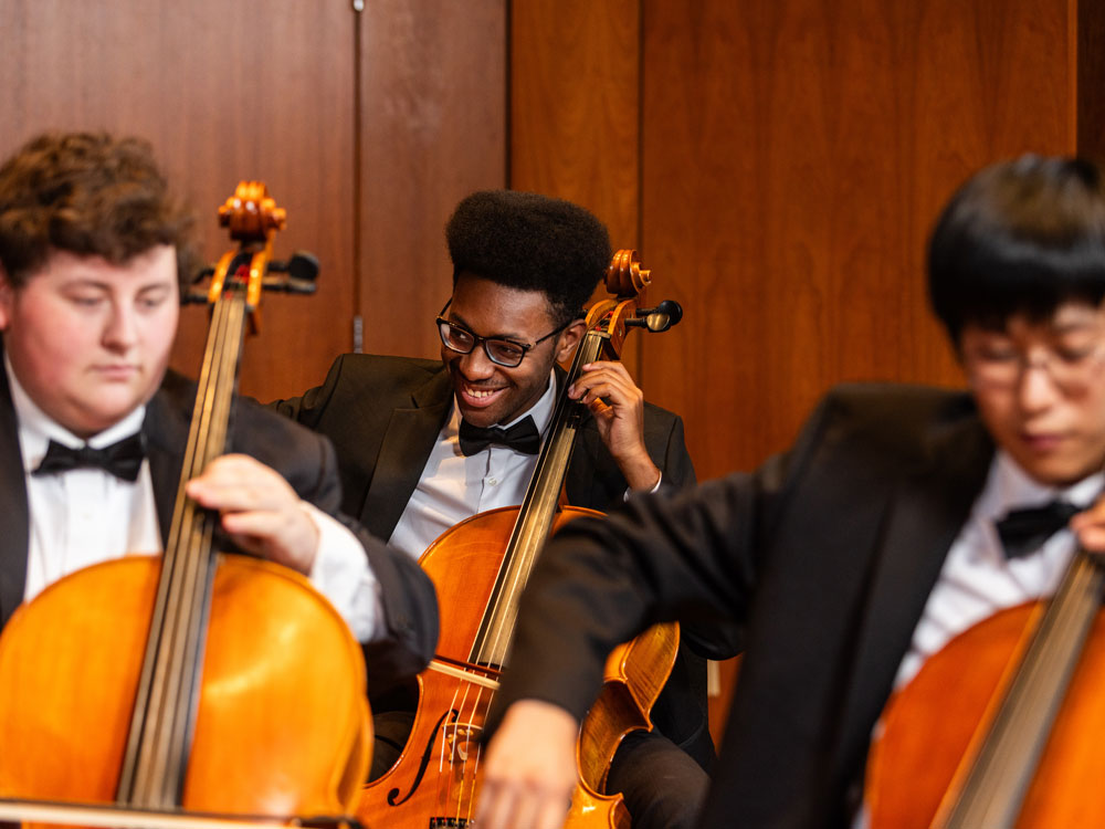 A group of Georgia Southern cello players perform in a concert hall with other stringed instruments.