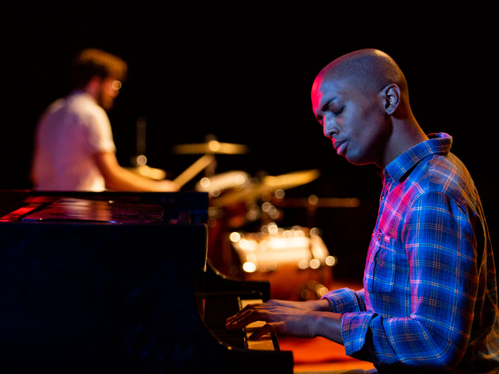 A Georgia Southern student plays piano with percussion in the background in a concert hall.