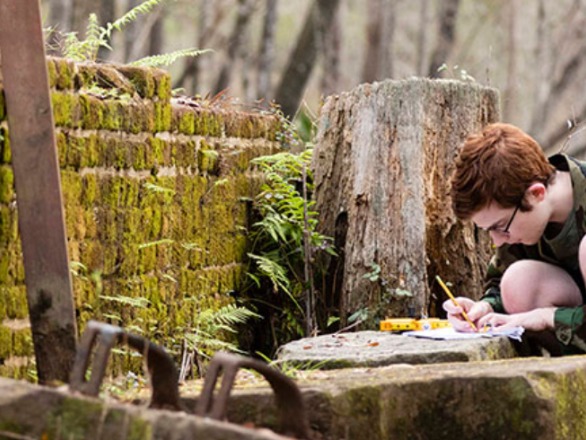 A history student doing fieldwork in some brick ruins in a forest.