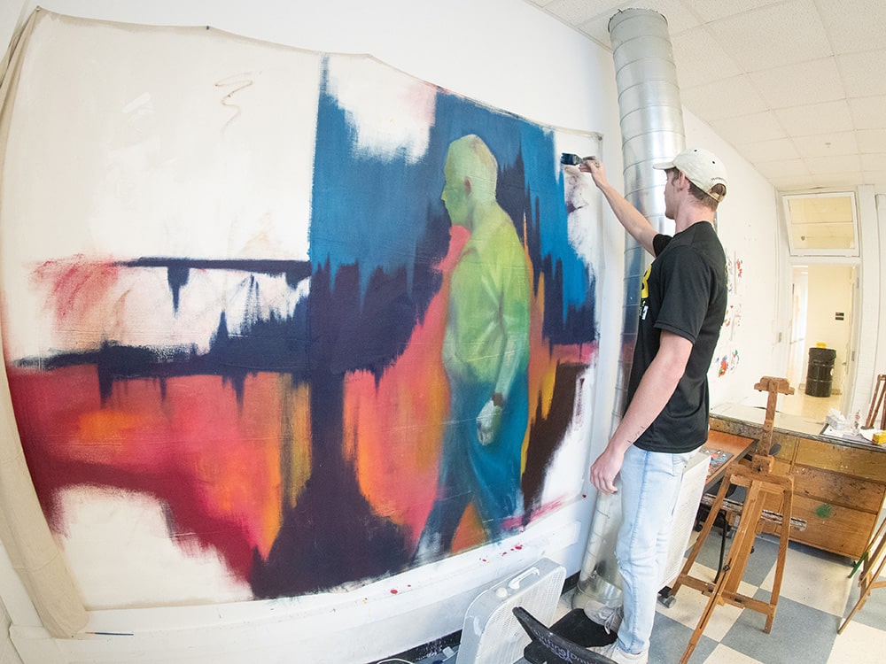 In one of Georgia Southern's studio spaces, a student stands to paint on a large canvas tacked to a wall
