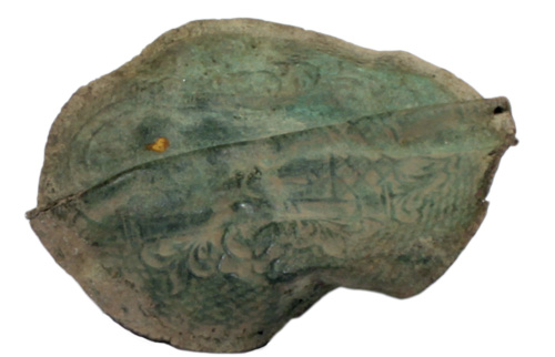 An irregular lumpy piece of corroded brass with some markings embossed on it.