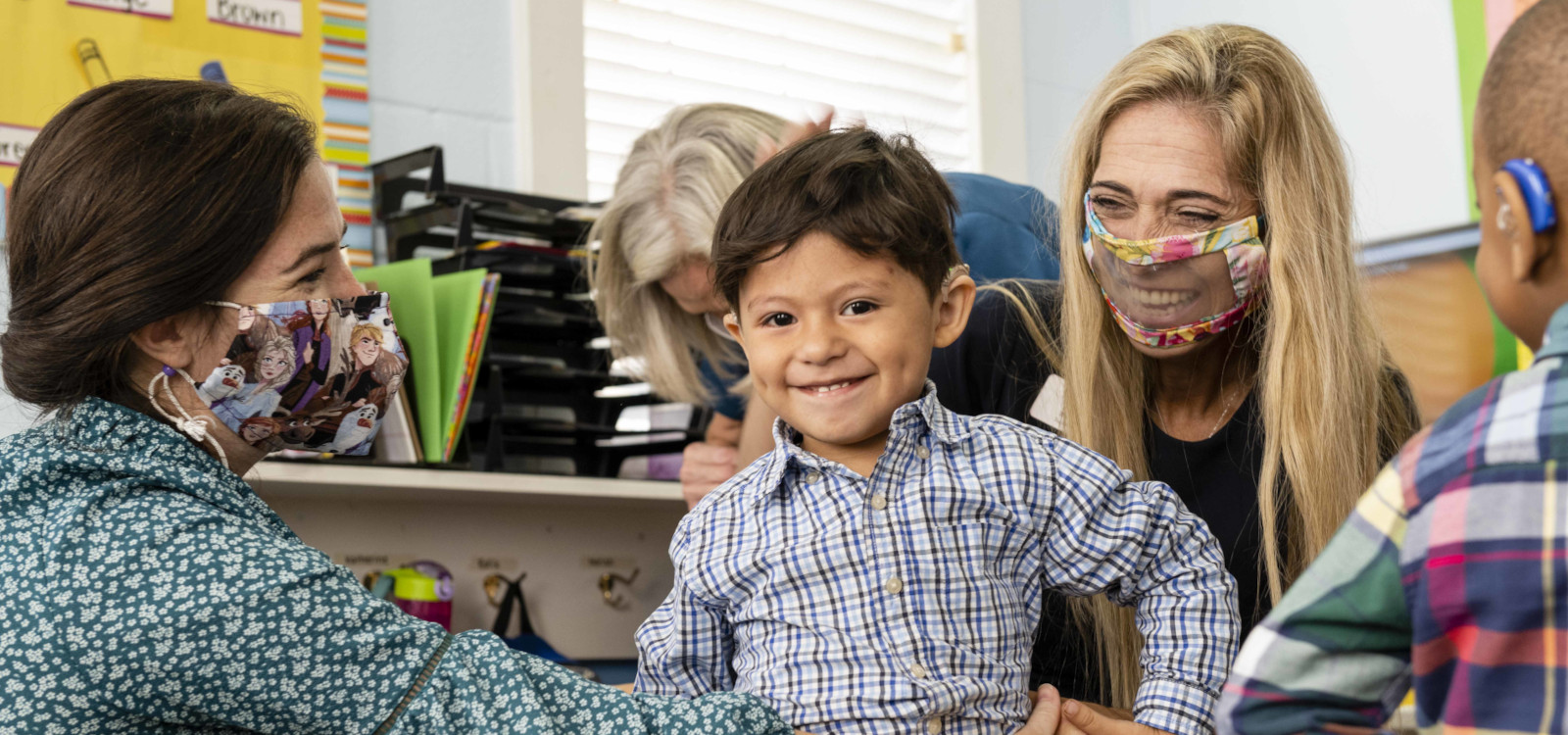 A group of speech pathologists interact with young children wearing hearing aids.