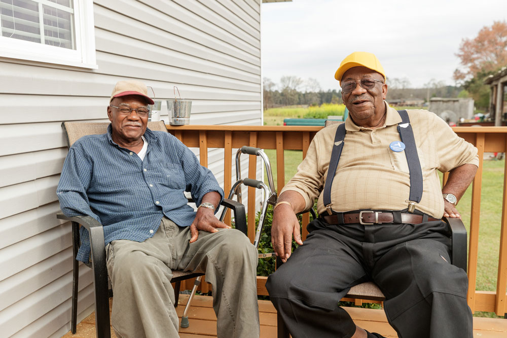 Two elderly men sitting on a porch and smiling at the camera