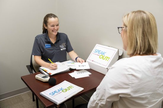 A SPEAK OUT participant meets with a speech therapist in a one-on-one sessions. They are using SPEAK OUT-branded workbooks and other materials.