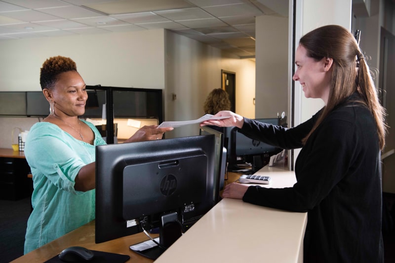 A woman handing a piece of paper to another woman behind a desk