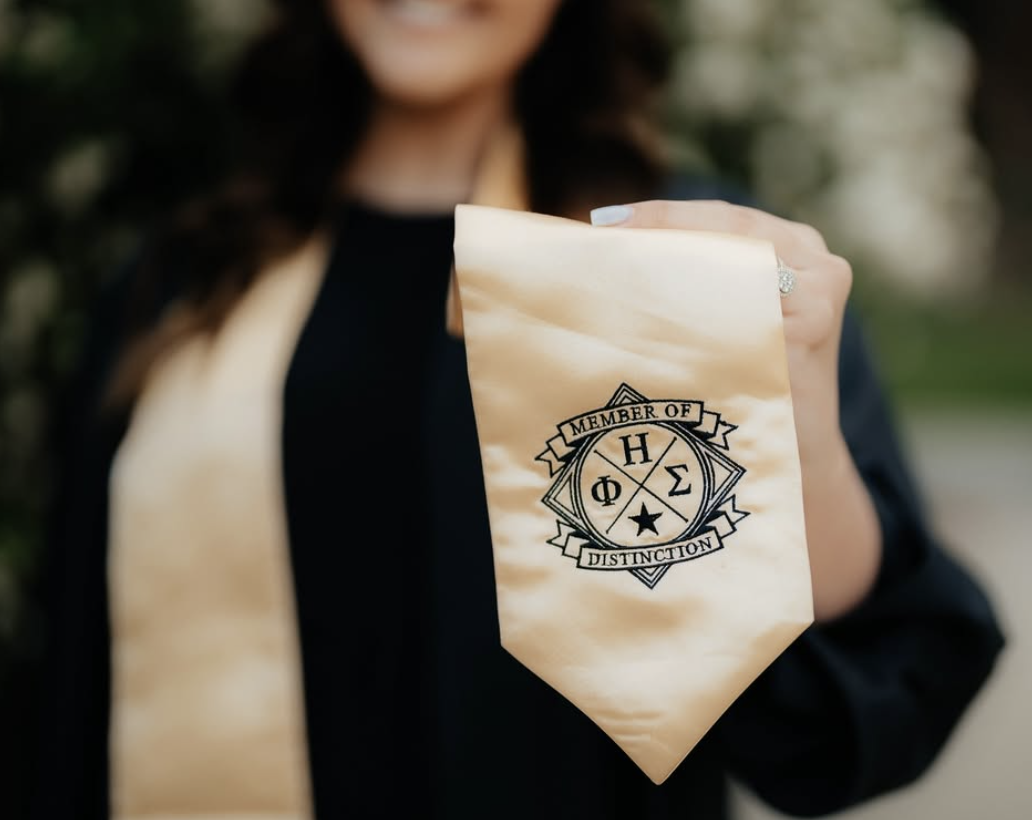 A graduate proudly displays a stole with the Phi Eta Sigma logo on it.