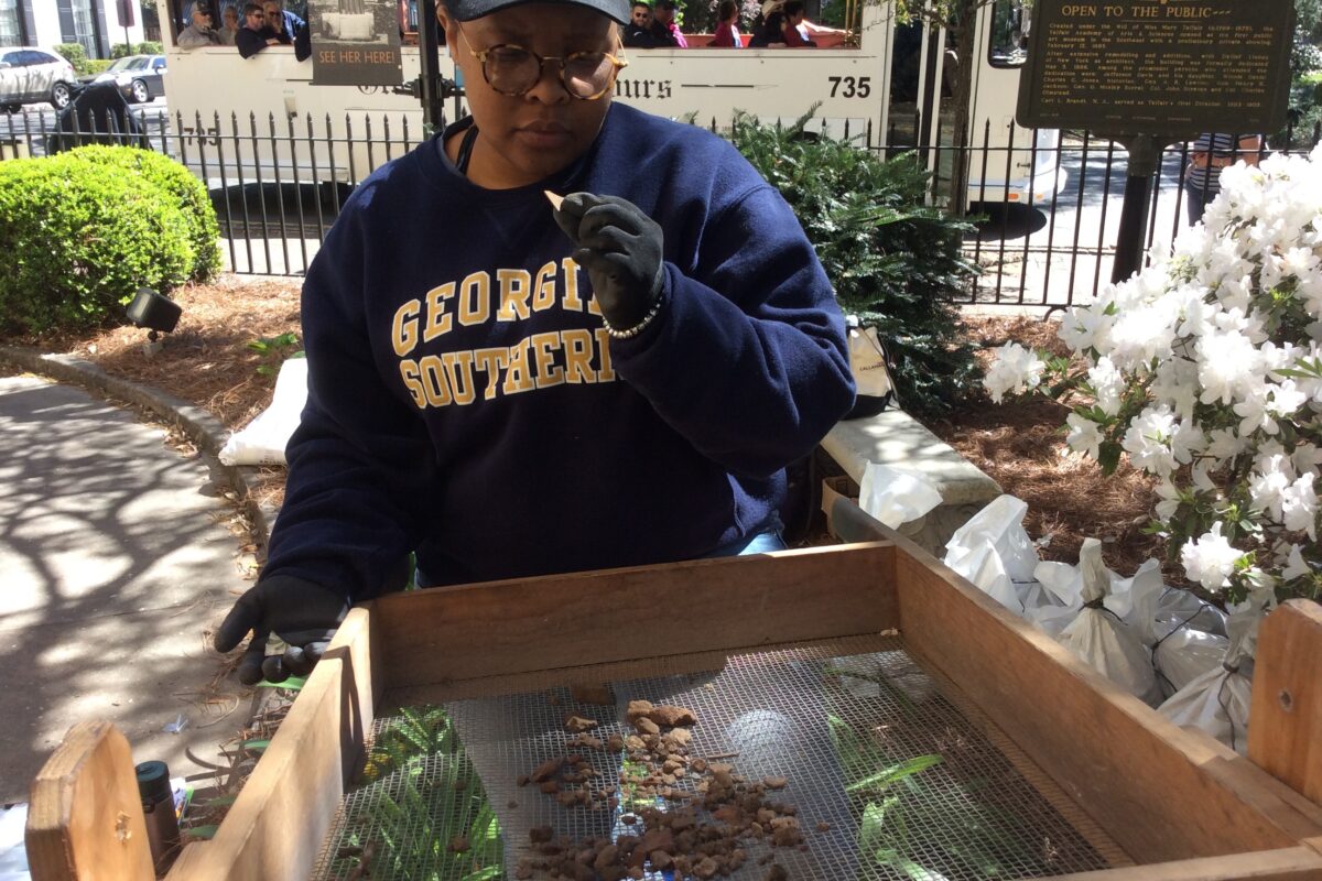 A Georgia Southern student inspects a small artifact while screening material in the front garden of the Telfair Museum.