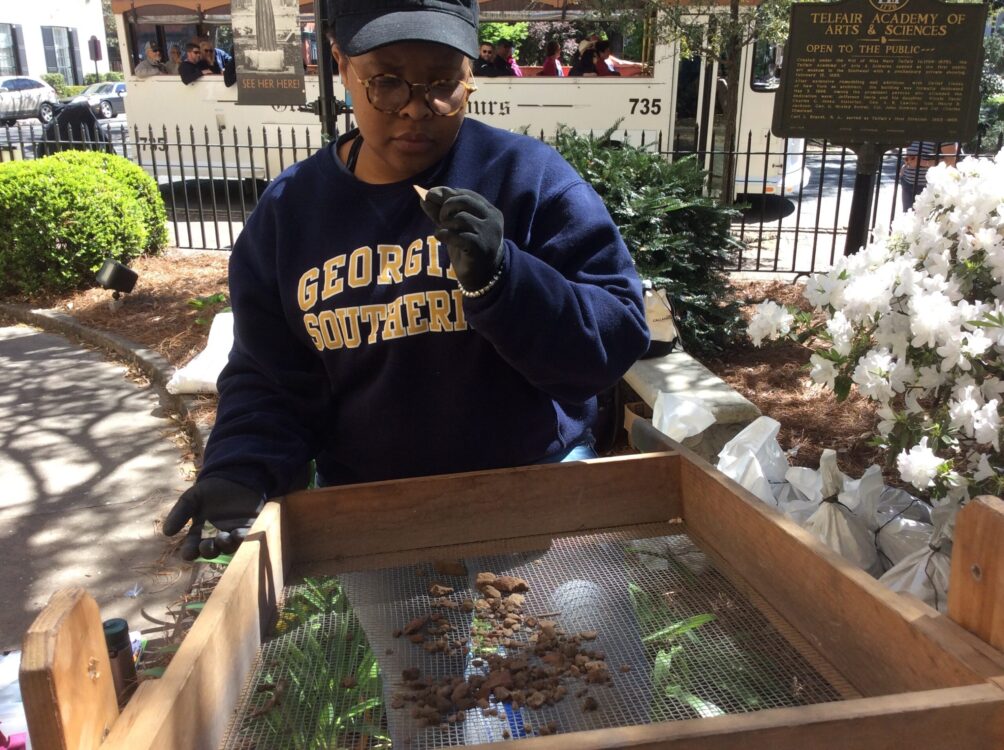 A Georgia Southern student inspects a small artifact while screening material in the front garden of the Telfair Museum.