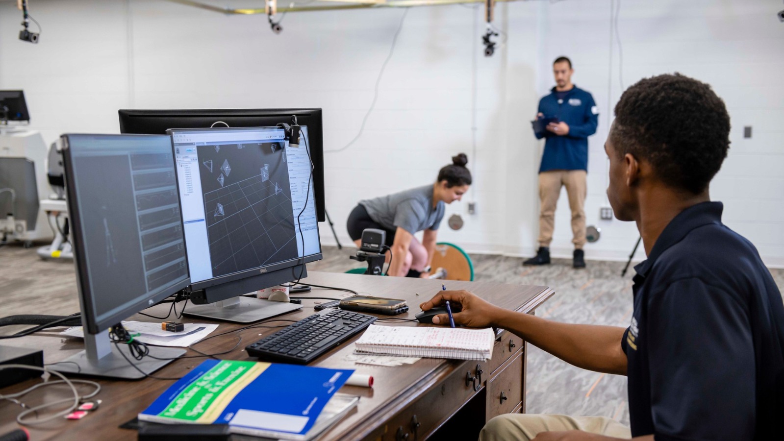 Student researchers monitor and measure the performance of a subject lifting weights.