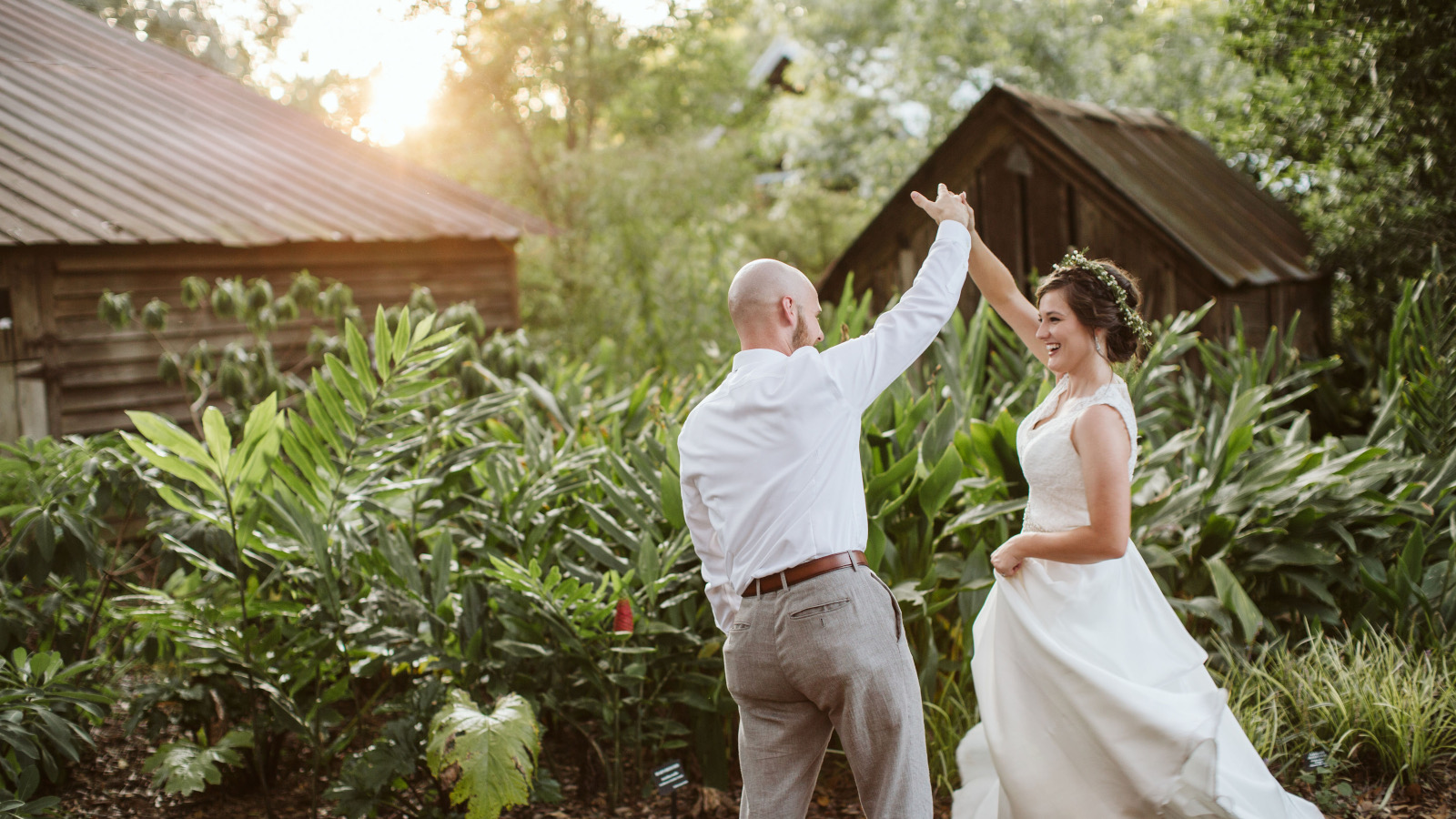 A newly wed couple dances in a garden with charmingly weathered old buildings in the background.