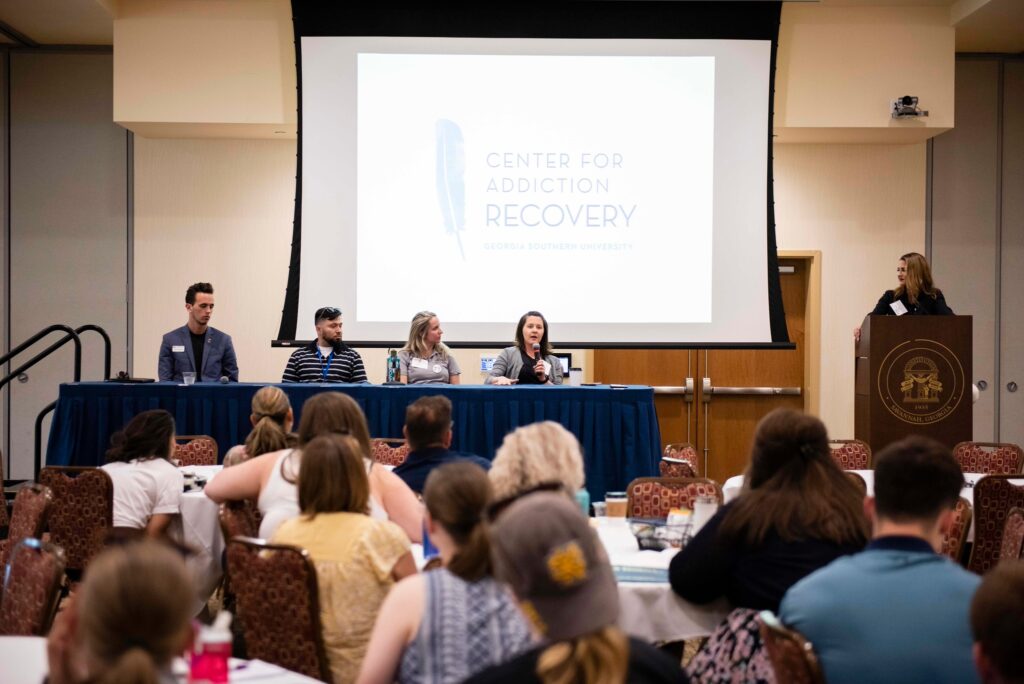 Four presenters speaking to a crowd of students about addiction