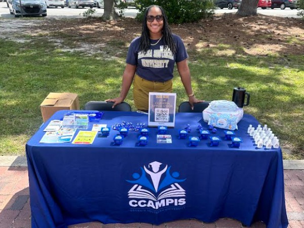 CCAMPIS representative stands behind an information table at a campus outdoor event.