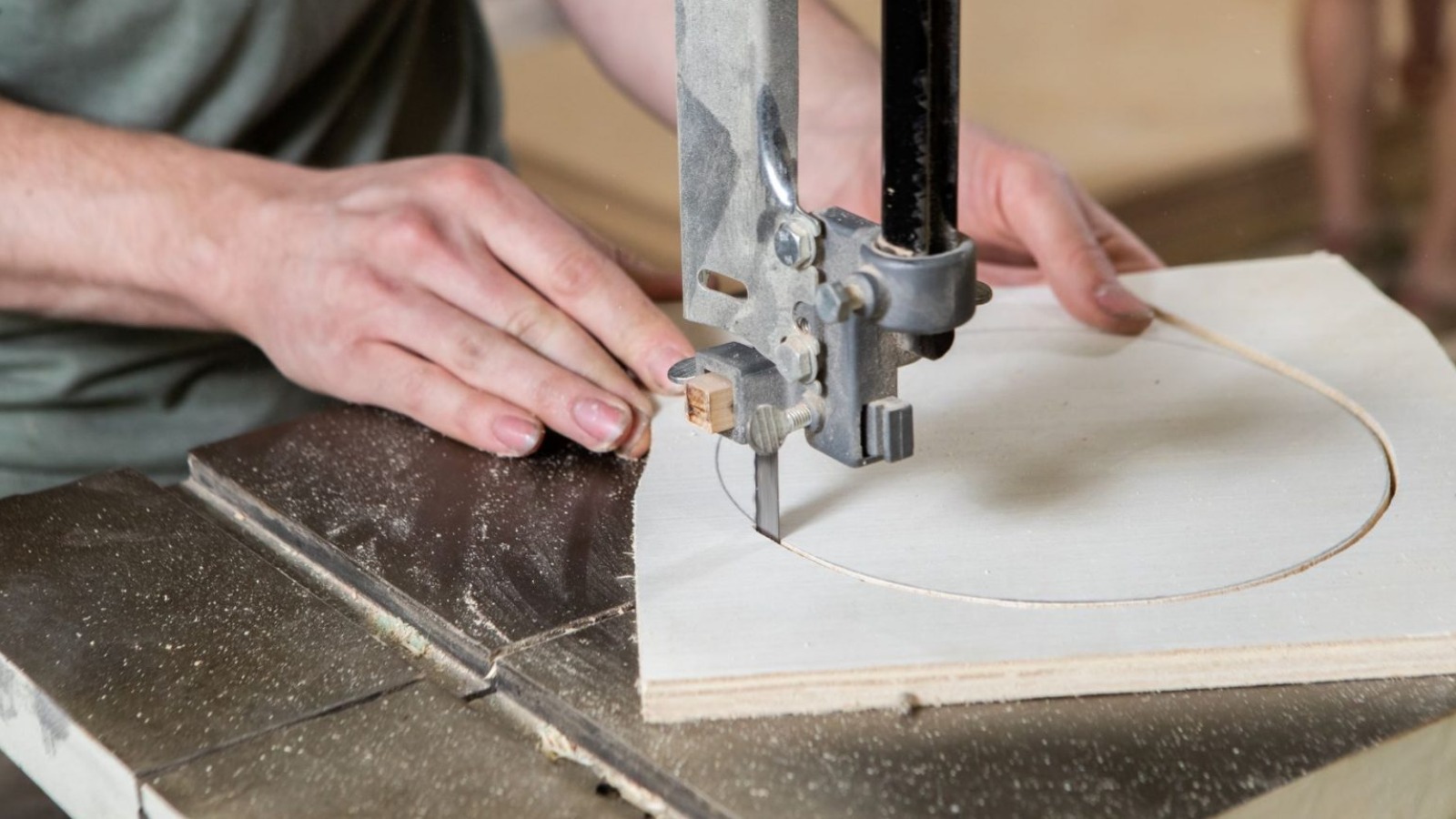 A fabricator uses a bandsaw to cut out a circle from a piece of plywood.