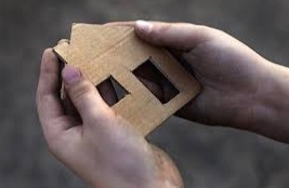 A person holds a cardboard cutout of a house